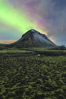 Aurora Borealis illuminates the sky above a snow-capped mountain in Iceland, with a mossy foreground under starlight. - ADSF51542