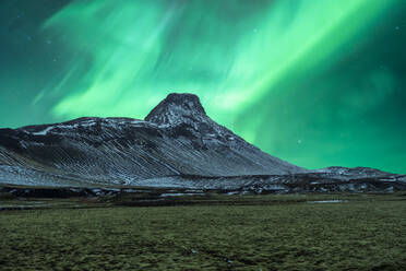 Vivid green Northern Lights dance above a snow-covered Icelandic peak under a night sky. - ADSF51543