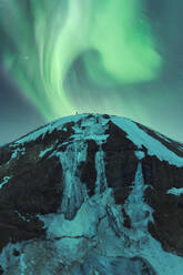 Spectacular aurora borealis swirls above a snow-covered peak in the serene Iceland night, offering an enchanting natural display. - ADSF51556