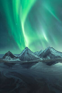 Captivating northern lights swirling above the majestic, snow-covered mountains under a starry sky in Iceland. - ADSF51558