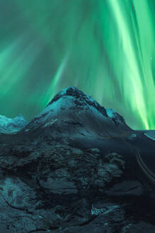 Enchanting aurora borealis dancing over a rugged Icelandic mountain peak at night, showcasing nature's light spectacle. - ADSF51559