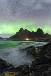 Spectacular northern lights (aurora borealis) dance above a rugged coastline with a towering mountain in the background Eystrahorn, Iceland - ADSF51574