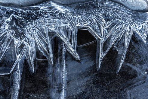 A close-up view of the captivating patterns formed by ice crystals on a dark frozen surface, highlighting nature's geometric artistry. - ADSF51584