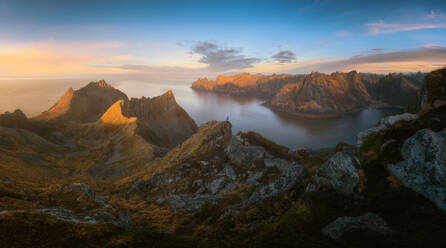 A serene mountainous landscape bathed in the warm glow of sunset with a lone hiker admiring the view in Senja, Norway - ADSF51588