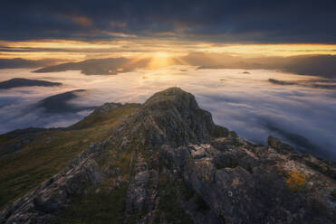 Capture the breathtaking beauty of remote hiker in a mountain peak bathed in sunrise glow, rising above a sea of clouds in Urkiola Natural Park, Spain - ADSF51589