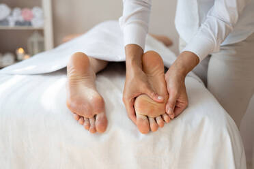 Crop hands of anonymous female therapist massaging foot of customer lying on bed to relieve pain by gently pressing pressure points at spa salon - ADSF51617