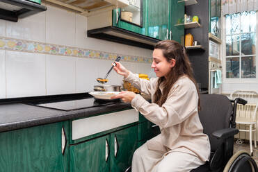 A smiling young woman in a wheelchair serves herself a healthy meal, showcasing independent living - ADSF51687