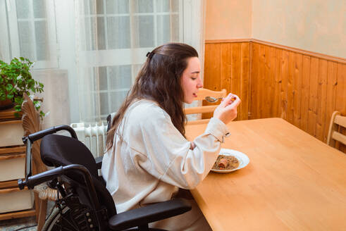 Content woman in a wheelchair enjoys a homemade meal at a dining table, exemplifying accessibility at home - ADSF51688
