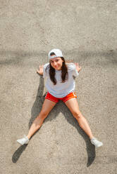 A fit young woman dressed in sportswear stretches on a concrete surface under the sun, exuding an active, healthy lifestyle vibe - ADSF51689