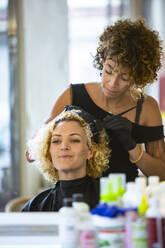 A curly-haired woman getting her hair dyed by a stylist in a salon, depicting a moment of beauty care. - ADSF51693