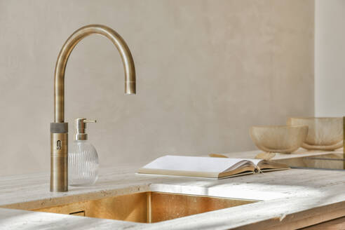 Curved faucet on sink besides open book at kitchen countertop in luxury contemporary apartment - ADSF51738