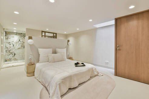 Illuminated spacious bedroom with tray on bed and shower booth in contemporary luxury apartment - ADSF51741