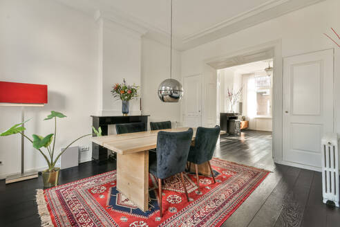 Pendant light hanging over wooden table and chairs in dining room of luxurious house with carpet and fireplace - ADSF51747