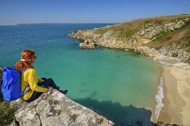 Frankreich, Bretagne, Wanderin sitzt auf der Kante mit Blick auf den Strand der Landzunge Cap Sizun - ANSF00678