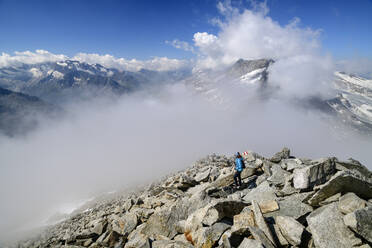 Austria, Tyrol, Female hiker ascending rocky slope of Hoher Riffler with thick fog in background - ANSF00719