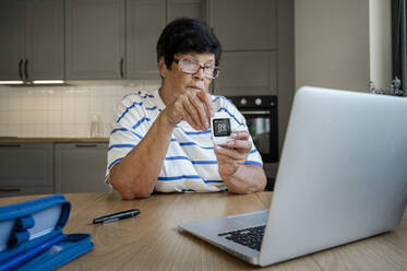 Ältere Frau zeigt Blutzuckermessgerät bei Videoanruf über Laptop - ALKF00928