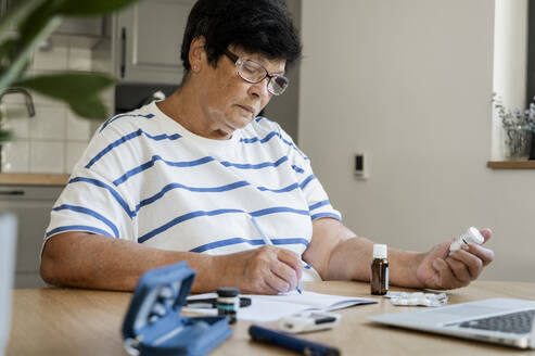 Ältere Frau macht sich Notizen über Medikamente durch Online-Konsultation zu Hause - ALKF00929