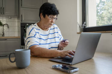 Ältere Frau beim Bezahlen mit Kreditkarte über einen Laptop zu Hause - ALKF00930