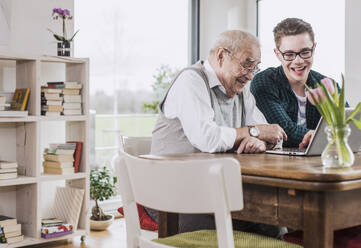 Glücklicher junger Mann, der seinem Großvater zu Hause Laptop-Unterricht gibt - UUF30854