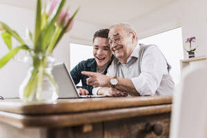 Glücklicher älterer Mann und Enkel im Gespräch über Videoanruf durch Laptop - UUF30855