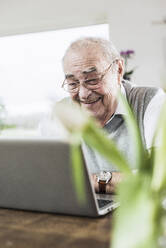 Lächelnder älterer Mann, der einen Videoanruf über einen Laptop zu Hause führt - UUF30856