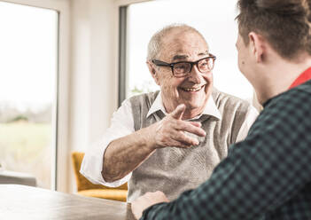 Happy senior man gesturing and talking to grandson at home - UUF30858