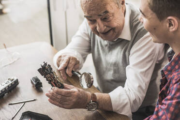 Glücklicher älterer Mann zeigt seinem Enkel zu Hause eine Miniatur-Spielzeugeisenbahn - UUF30860