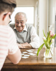 Happy grandfather playing cards with grandson at home - UUF30867