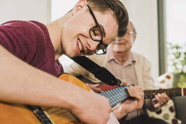 Glücklicher junger Mann, der mit seinem Großvater zu Hause Gitarre spielt - UUF30875