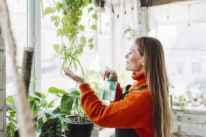 Botanist with long hair spraying water on plants in store - OLRF00023