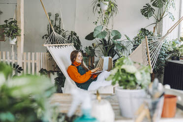 Botanist using laptop on hammock in plant store - OLRF00047