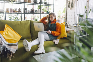 Botanist working with laptop on sofa in plant store - OLRF00060