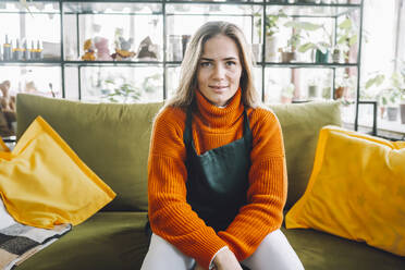 Smiling botanist sitting on sofa in plant store - OLRF00064