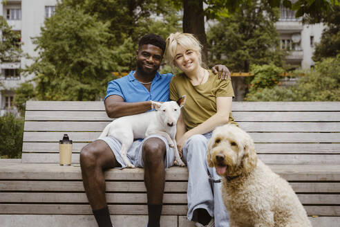 Portrait of smiling heterosexual couple with dogs in public park - MASF41424