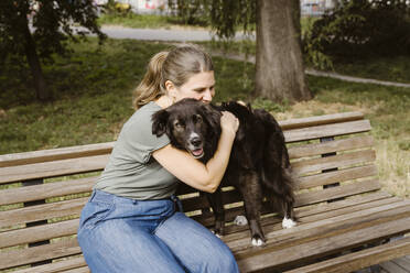 Mature woman embracing dog on bench in park - MASF41455