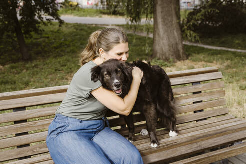 Mature woman embracing dog on bench in park - MASF41455