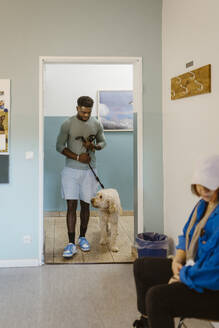 Young man walking labradoddle while waiting in veterinary clinic - MASF41471