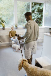 Young man walking with dog in waiting room of vet medical clinic - MASF41472