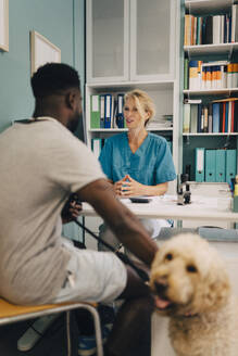 Young man with dog talking to female veterinarian at desk in medical clinic - MASF41480