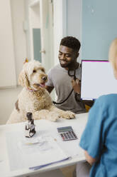 Smiling man with labradoddle looking at female vet in animal hospital - MASF41481