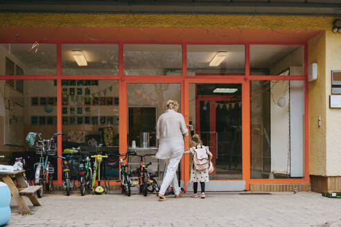Senior woman with granddaughter standing near door of kindergarten - MASF41510
