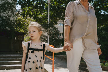 Senior woman holding hands while walking with granddaughter at kindergarten - MASF41513