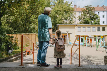 Senior man with granddaughter standing near railing at kindergarten - MASF41516