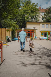 Grandfather with granddaughter walking on footpath towards kindergarten - MASF41517