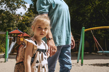 Portrait of girl holding hands while standing with grandfather at kindergarten - MASF41518