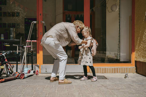 Senior woman tickling granddaughter while standing near door of kindergarten - MASF41519