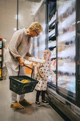 Senior woman holding basket while buying groceries with granddaughter at store - MASF41536