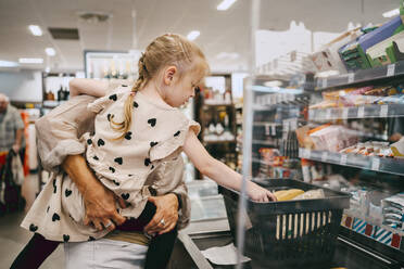 Senior woman carrying granddaughter at checkout counter in supermarket - MASF41540