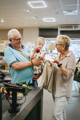 Girl assisting grandparents standing near checkout counter in supermarket - MASF41545