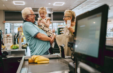 Happy granddaughter having fun with grandparents while shopping at supermarket - MASF41546